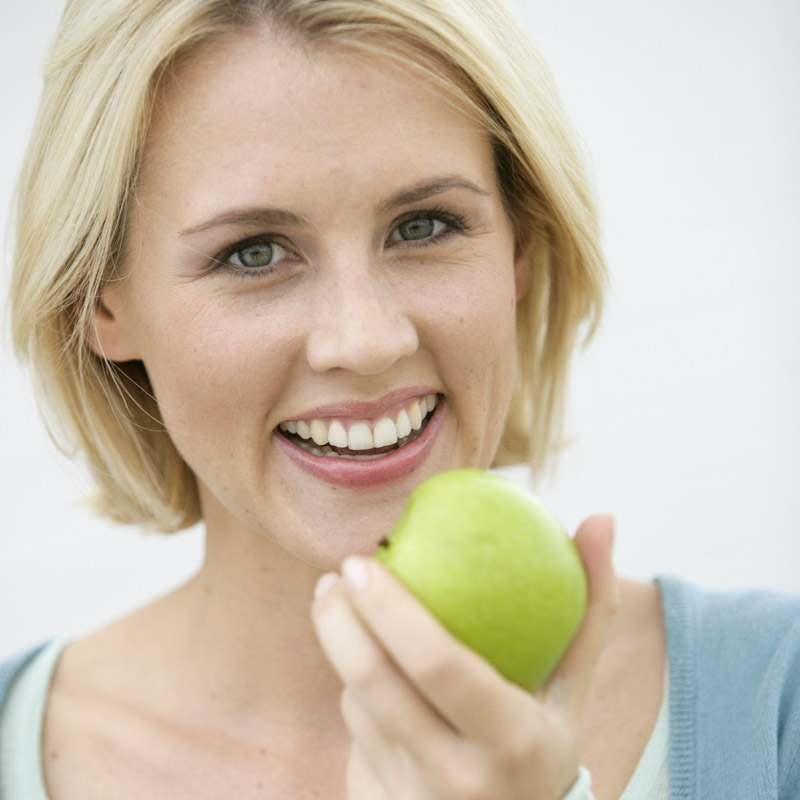 Eine blonde Frau mit schönen und
gesunden Zähnen beißt gleich in einen Apfel.